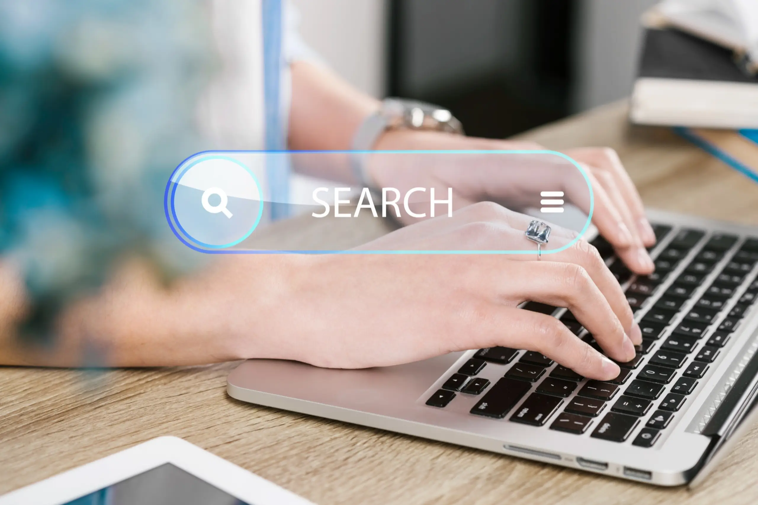 A person typing on a laptop keyboard with a search bar overlay displaying the text search and a magnifying glass icon